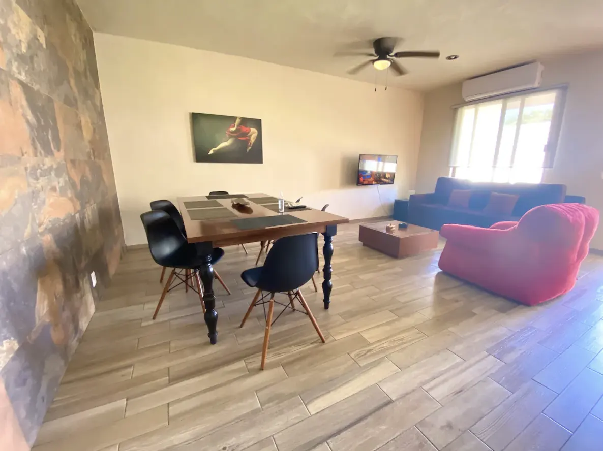 Spacious living-dining room with natural stone wall, wooden dining table and red armchair at Villa La Ceiba